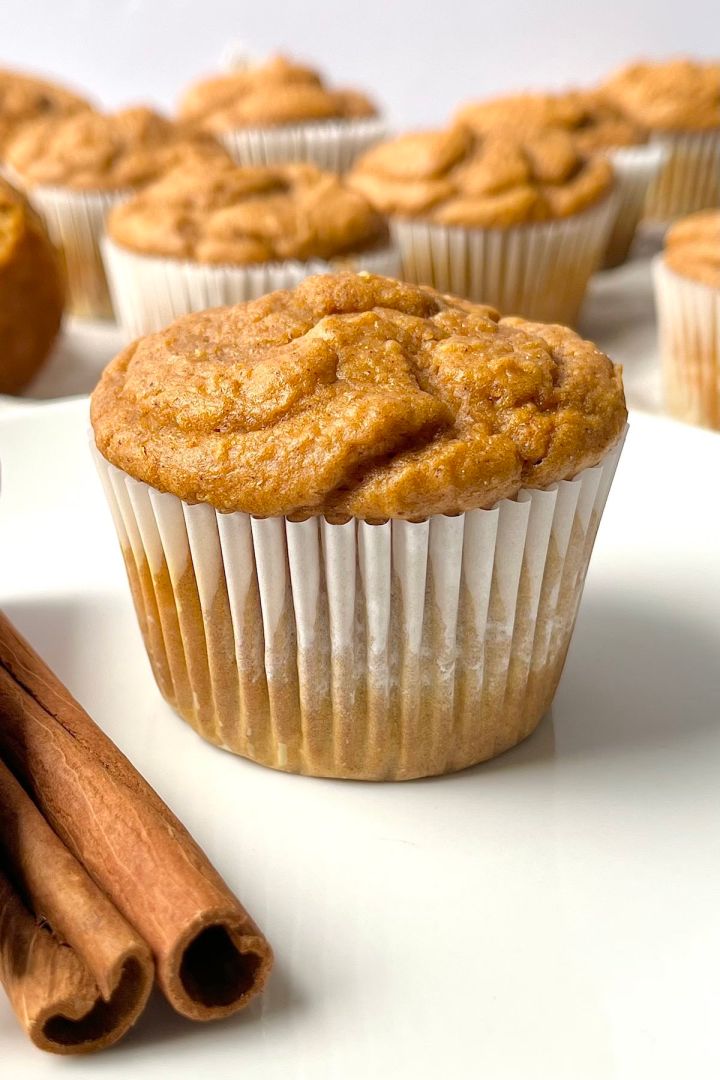 A pumpkin muffin on a white plate with the rest of the 3 Ingredient Pumpkin Muffins with Cake Mix scattered in the background.