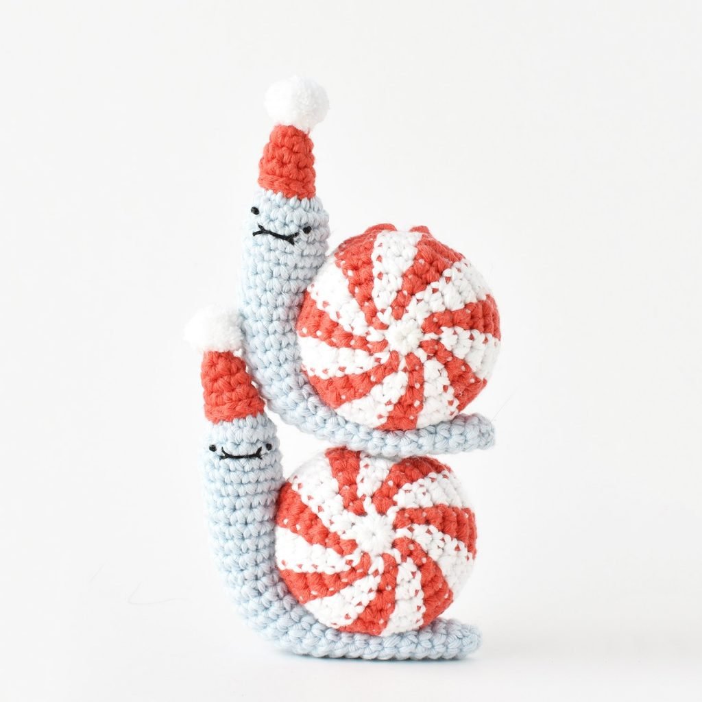 Image showing two completed amigurumi Peppermint Party Snails stacked up. Picture is within the Peppermint Party Snail free Christmas ornament crochet pattern on the Tiny Curl amigurumi crochet website.